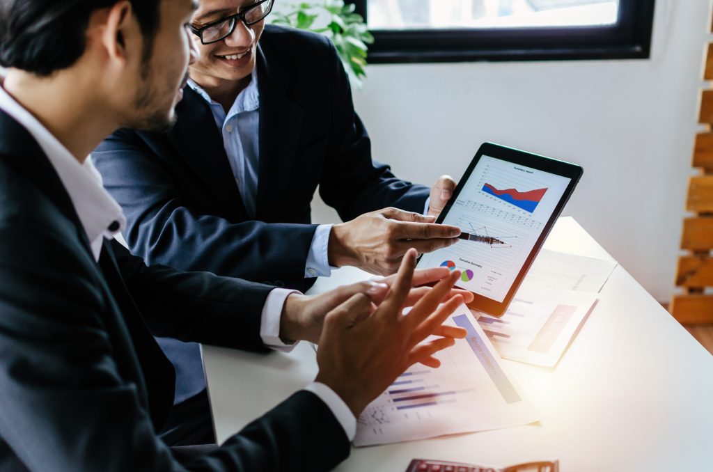 Jovem parceiro empresário homem investidor falando sobre informações do gráfico de estatísticas financeiras em tablet móvel juntos sentados na sala de reuniões no escritório, finanças, investimento e conceito de tecnologia digital
